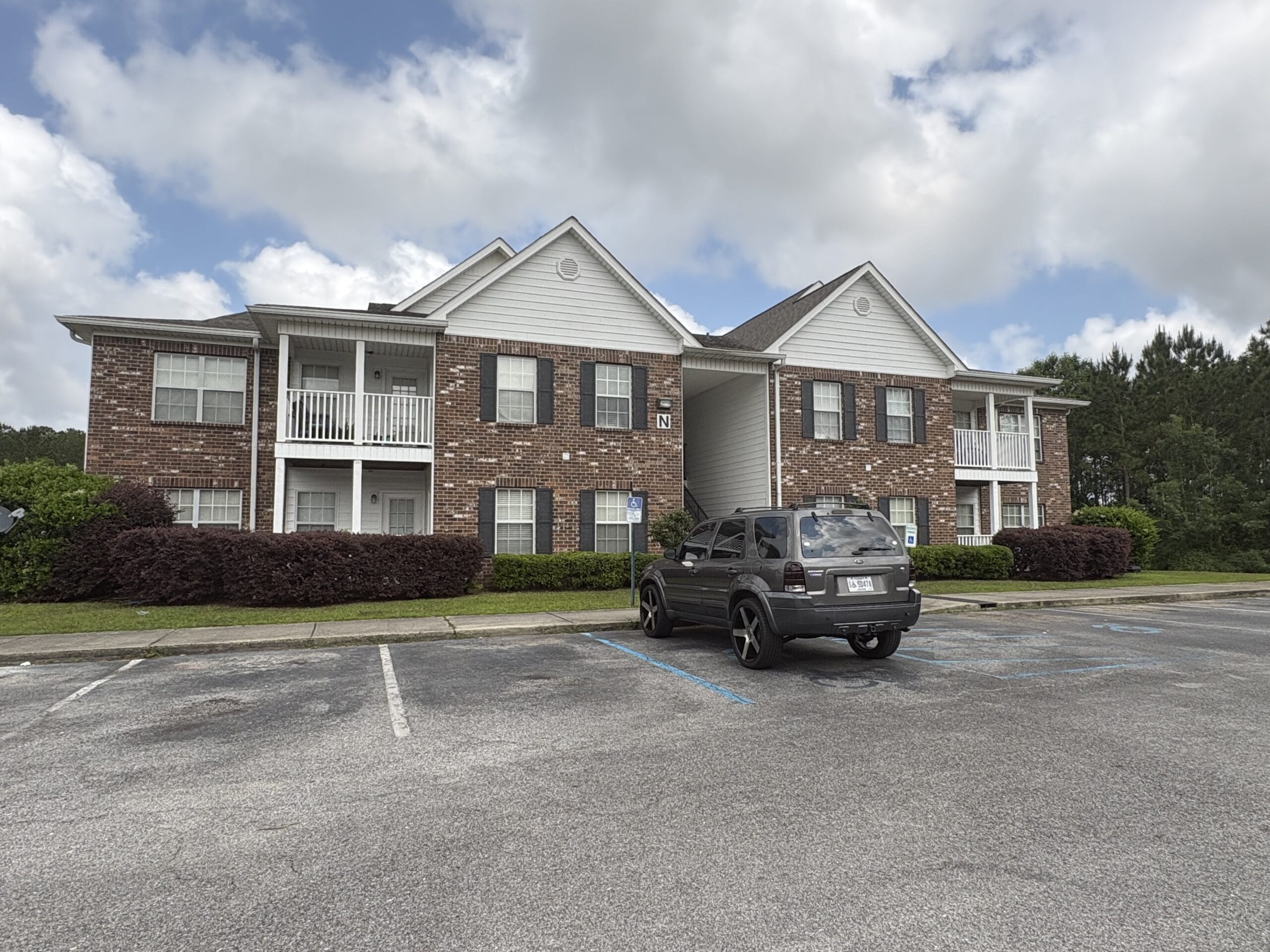 Exterior view of Bayou Village apartment buildings with brick facades, balconies, landscaped shrubs, and resident parking spaces.