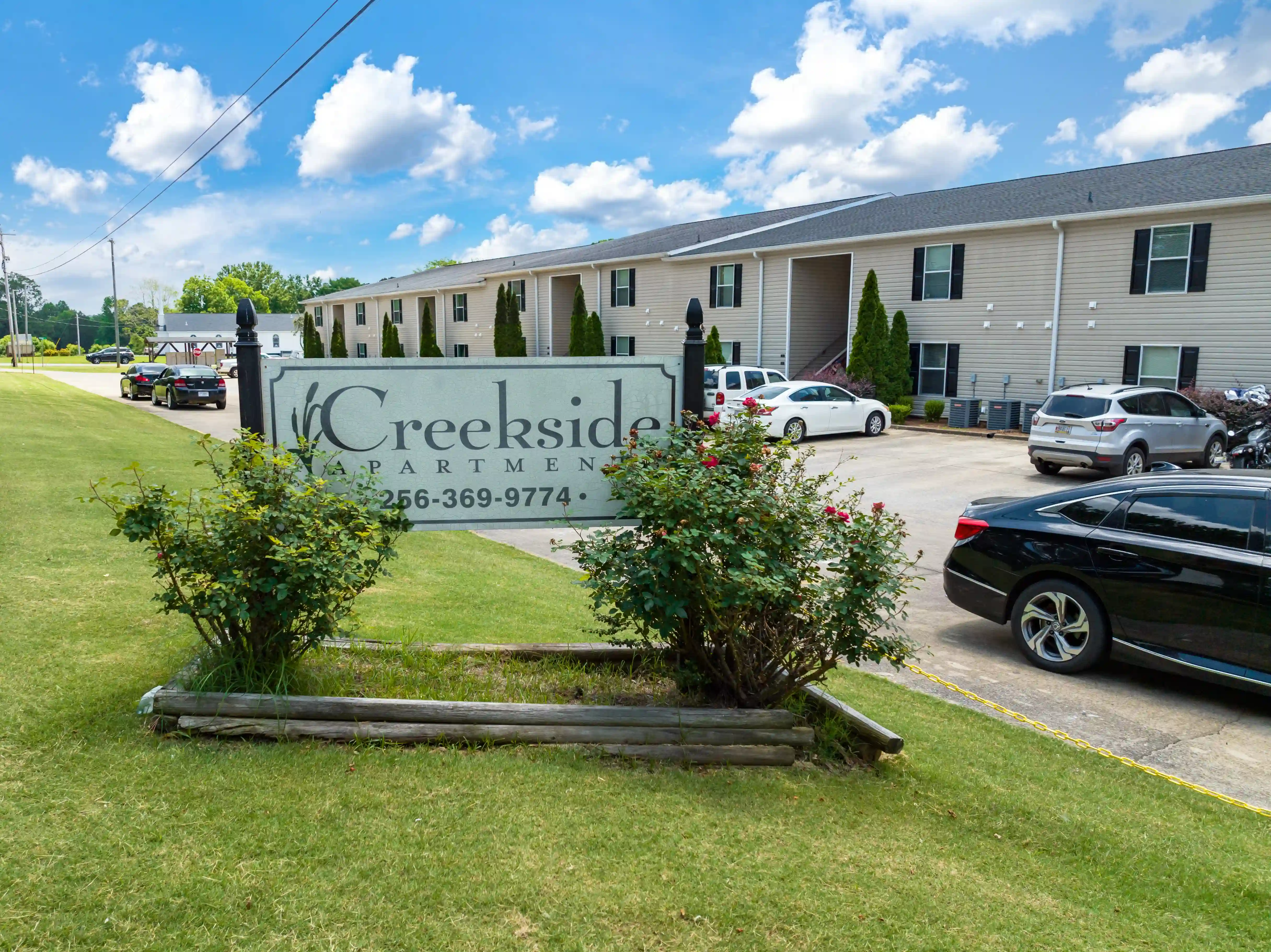 Exterior view of Creekside Apartments featuring the community entrance sign, apartment buildings, landscaped grounds, and resident parking area.