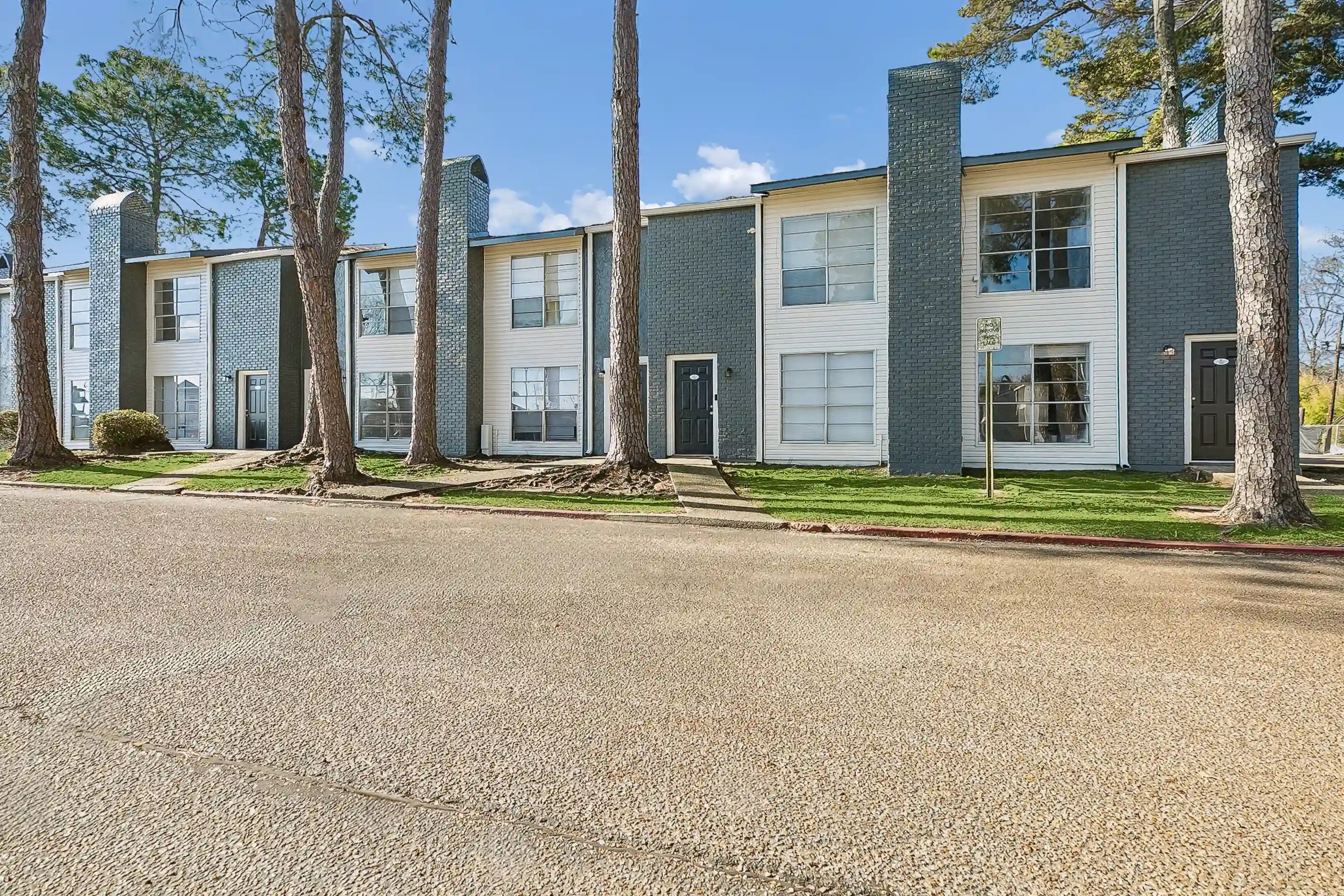 Exterior view of Greenview East apartment homes with modern townhome-style units, tall pine trees, sidewalks, and landscaped grounds.