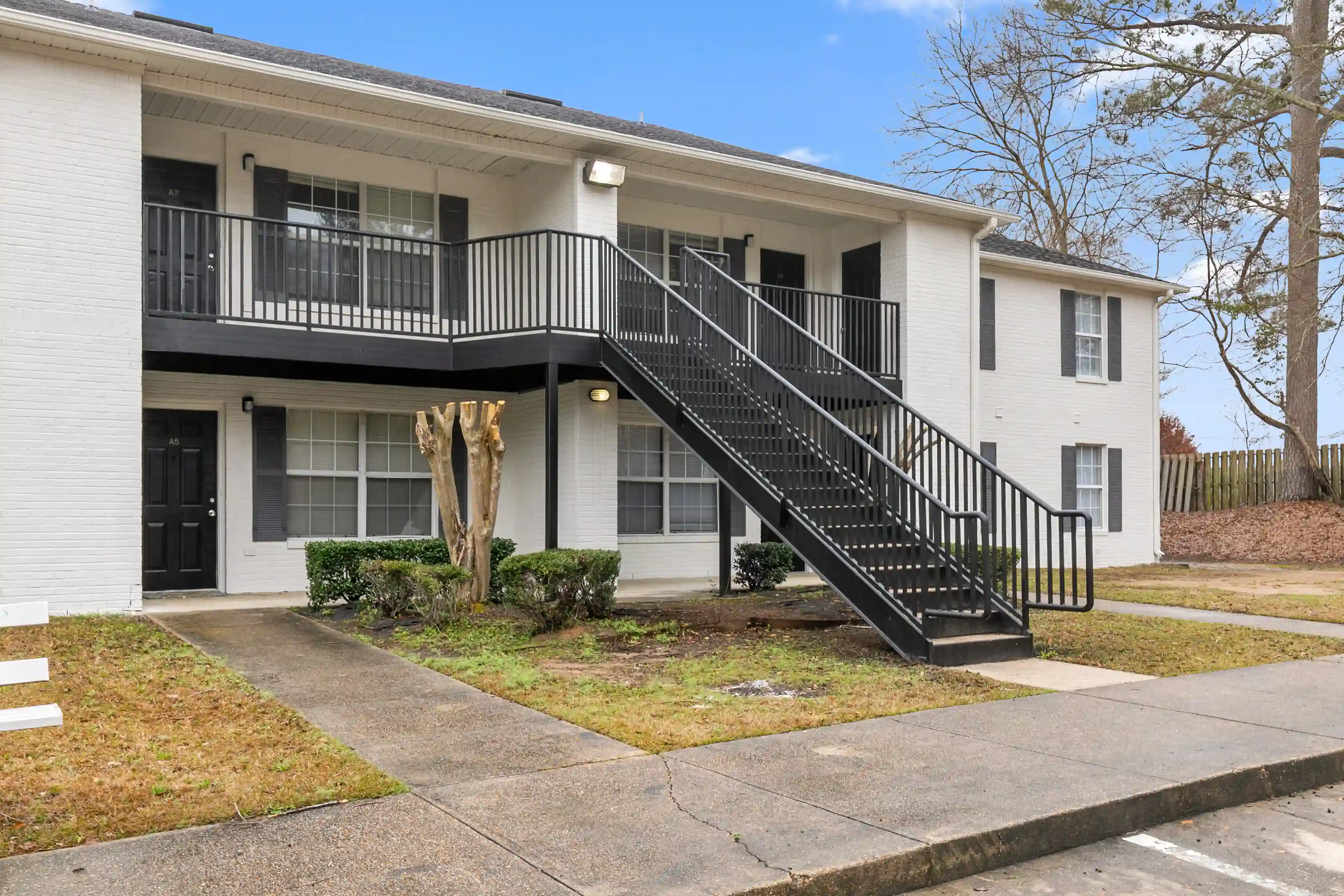 Exterior view of Pebble Creek Apartments featuring white brick residential buildings, black stair railings, landscaped walkways, and apartment entrances.