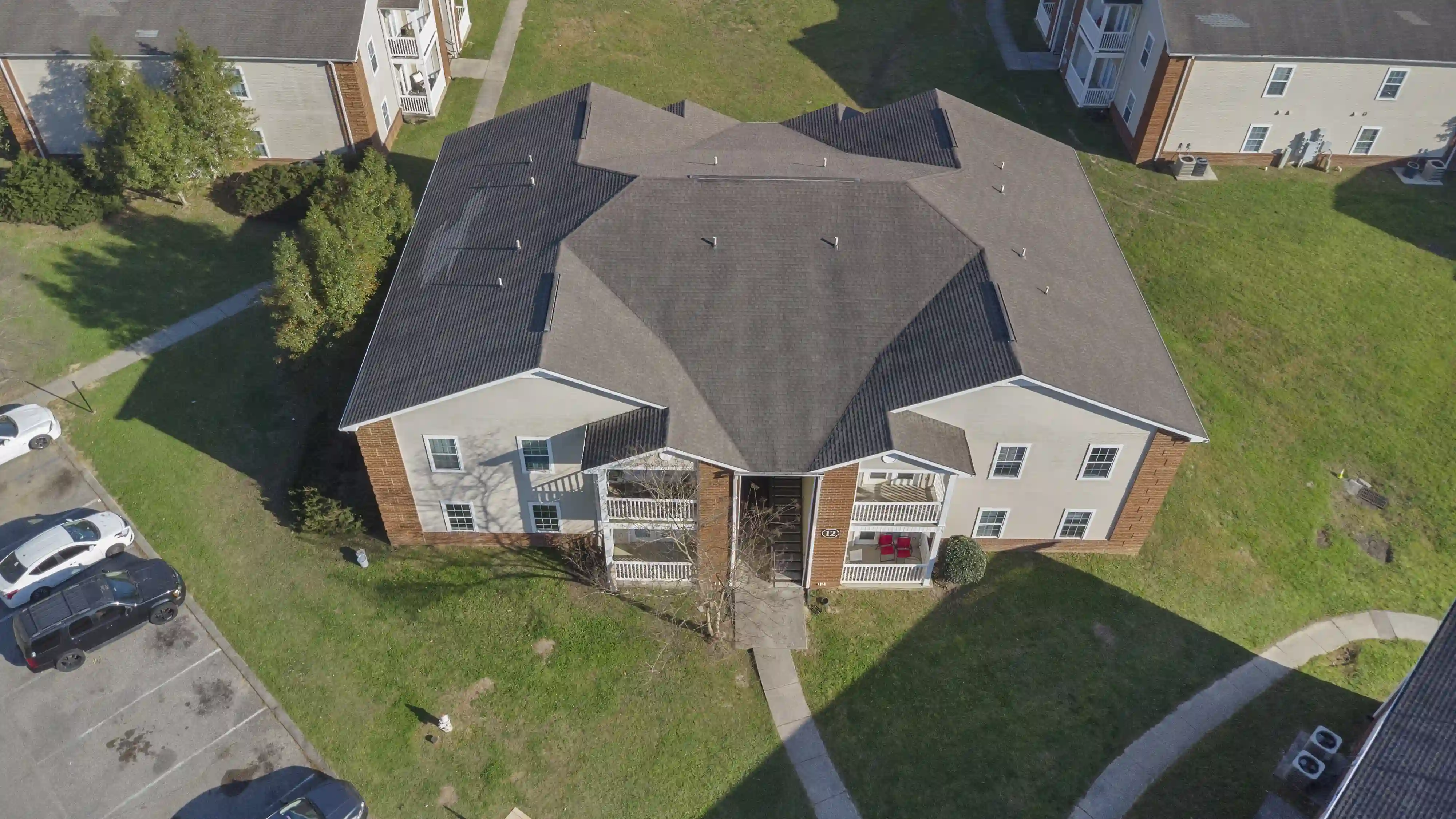 Aerial drone view of a Shadowood apartment building with balconies, landscaped grounds, sidewalks, and nearby resident parking spaces.