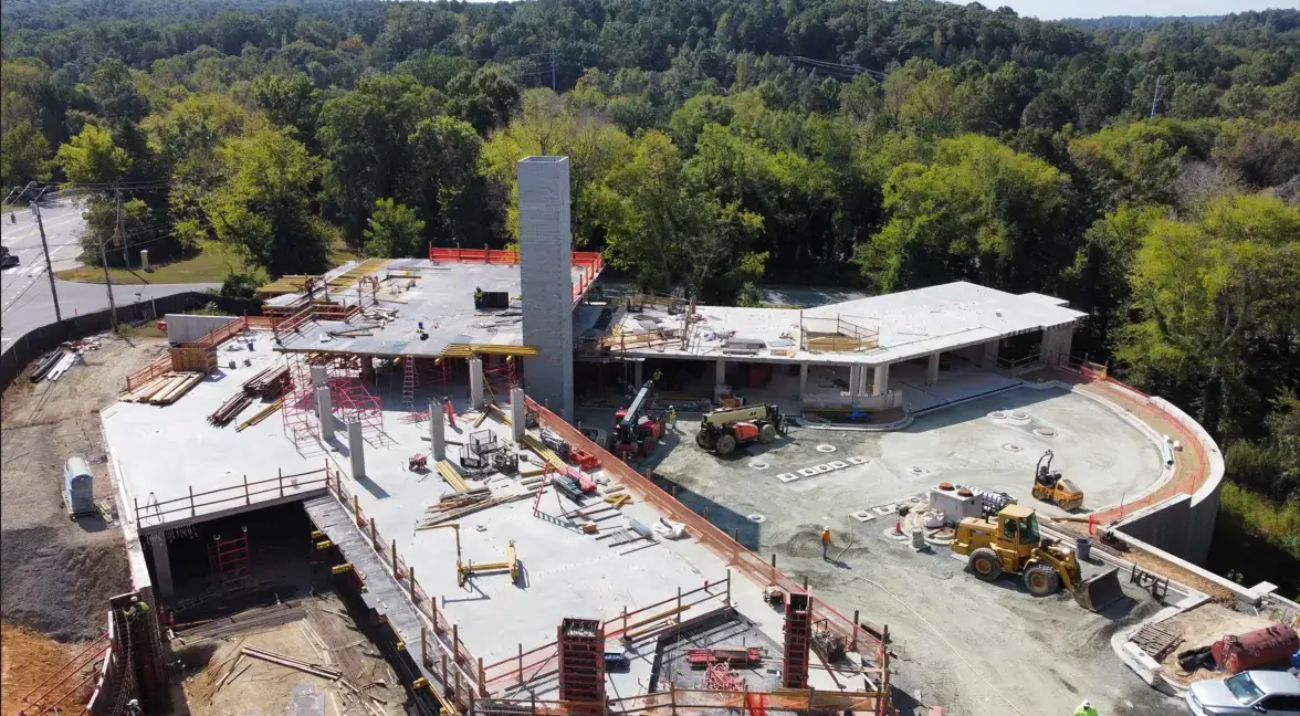 Aerial view of an active construction site at 1100 South Columbia Street showing concrete structures, construction equipment, workers, and surrounding trees.
