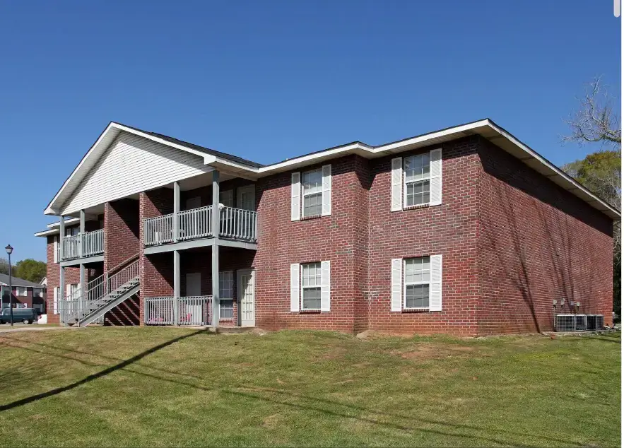 Exterior view of an affordable apartment building in Alabama featuring red brick walls, covered balconies, outdoor stairs, and a landscaped lawn.