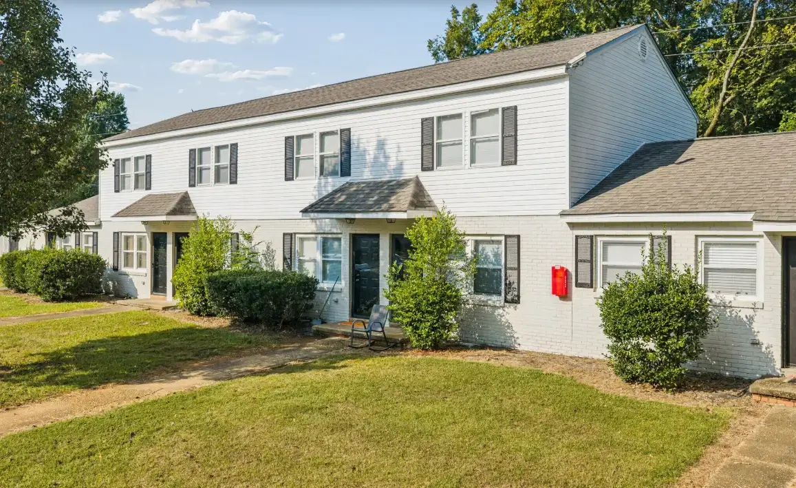 Exterior view of Bellview Apartments featuring white siding, brick accents, landscaped lawns, shrubs, sidewalks, and residential entrances.