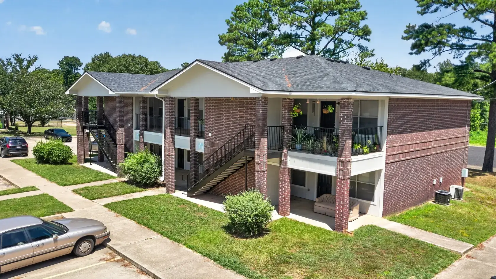 Exterior view of a Texas apartment community featuring brick buildings, covered balconies, landscaped lawns, walkways, and parking.