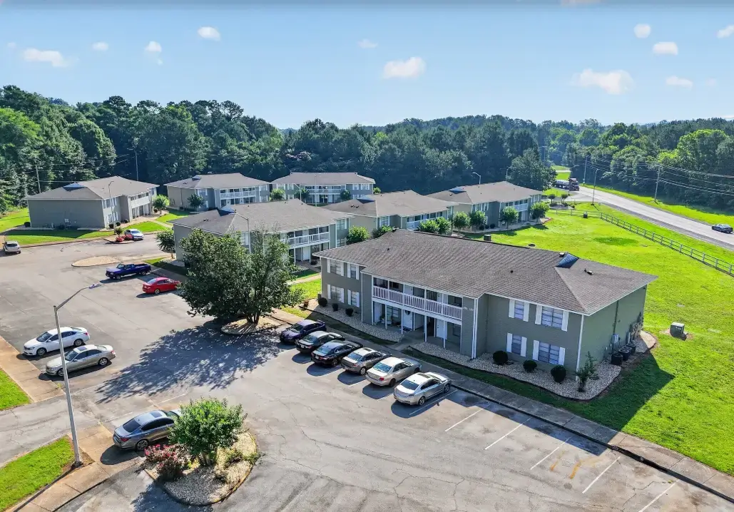 Aerial view of The Landings apartment community featuring multiple residential buildings, parking areas, landscaped grounds, mature trees, and a nearby road.