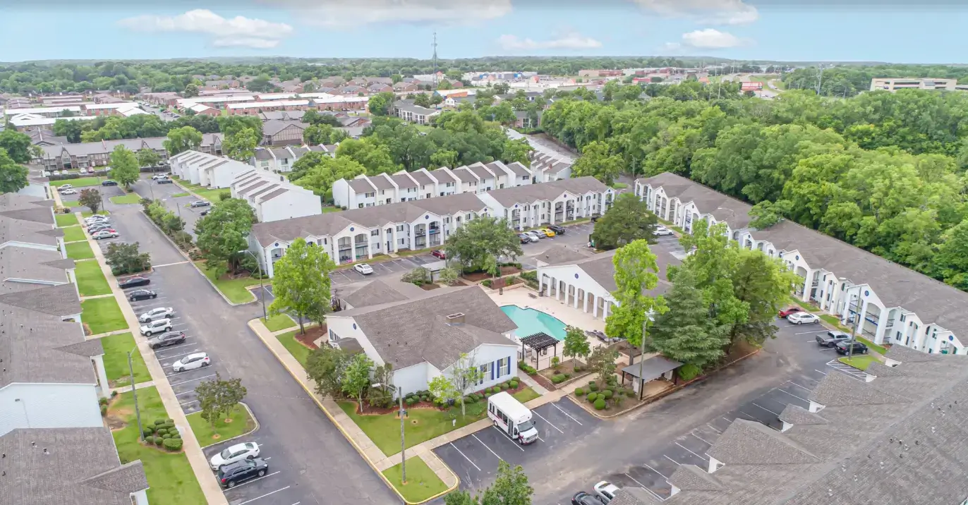 Aerial view of The Lofts on Fountain apartment community featuring residential buildings, parking areas, landscaped grounds, a swimming pool, and surrounding trees.